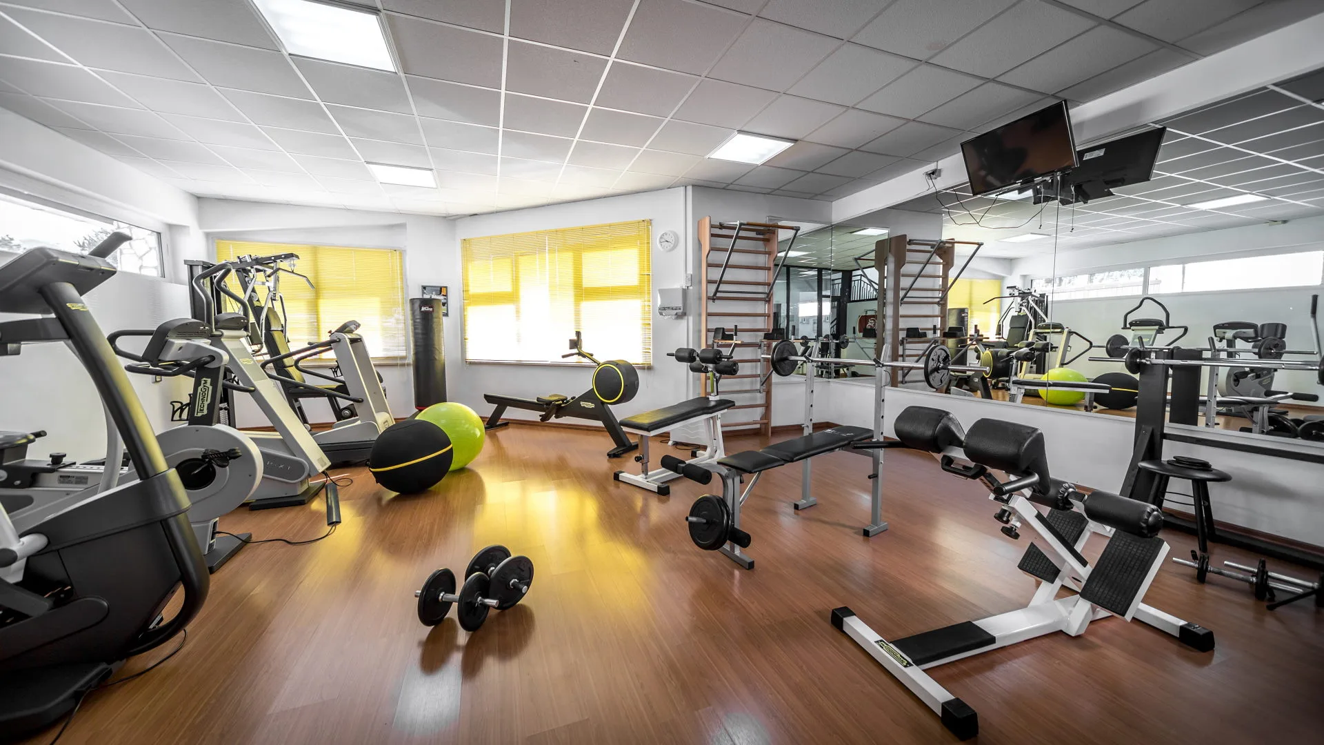 Sala fitness attrezzata con macchinari cardio, pesi, panche e specchi a parete