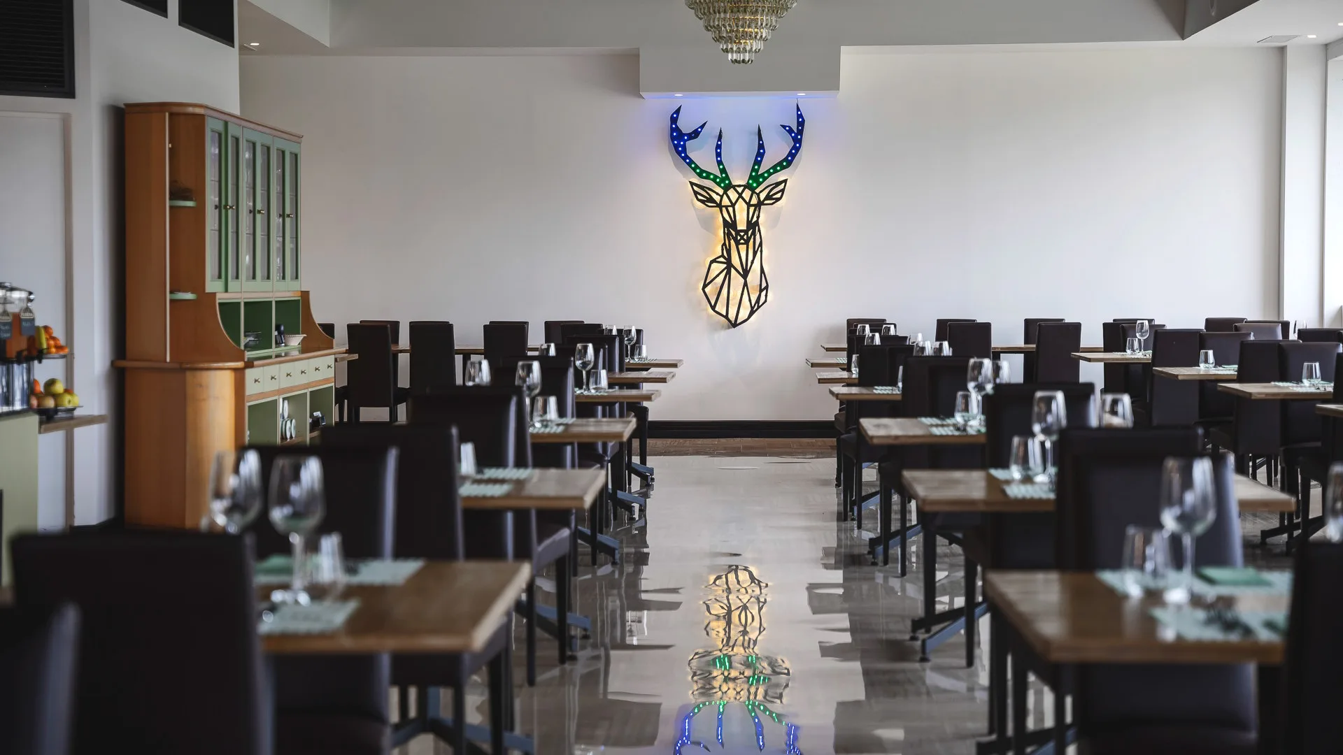 Sala ristorante con tavoli apparecchiati e decorazione a parete a forma di testa di cervo illuminata