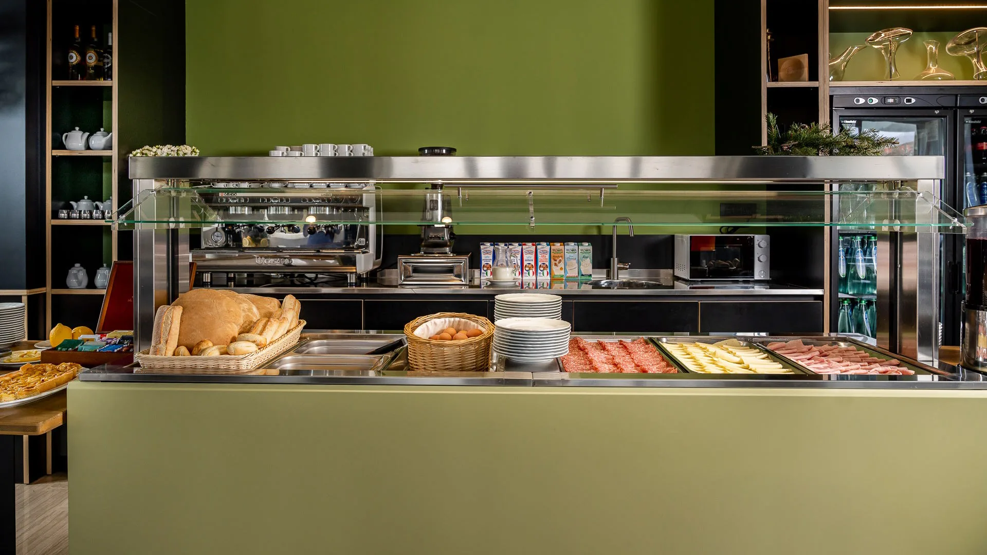 Banco buffet della colazione con pane, uova, salumi e formaggi su parete verde