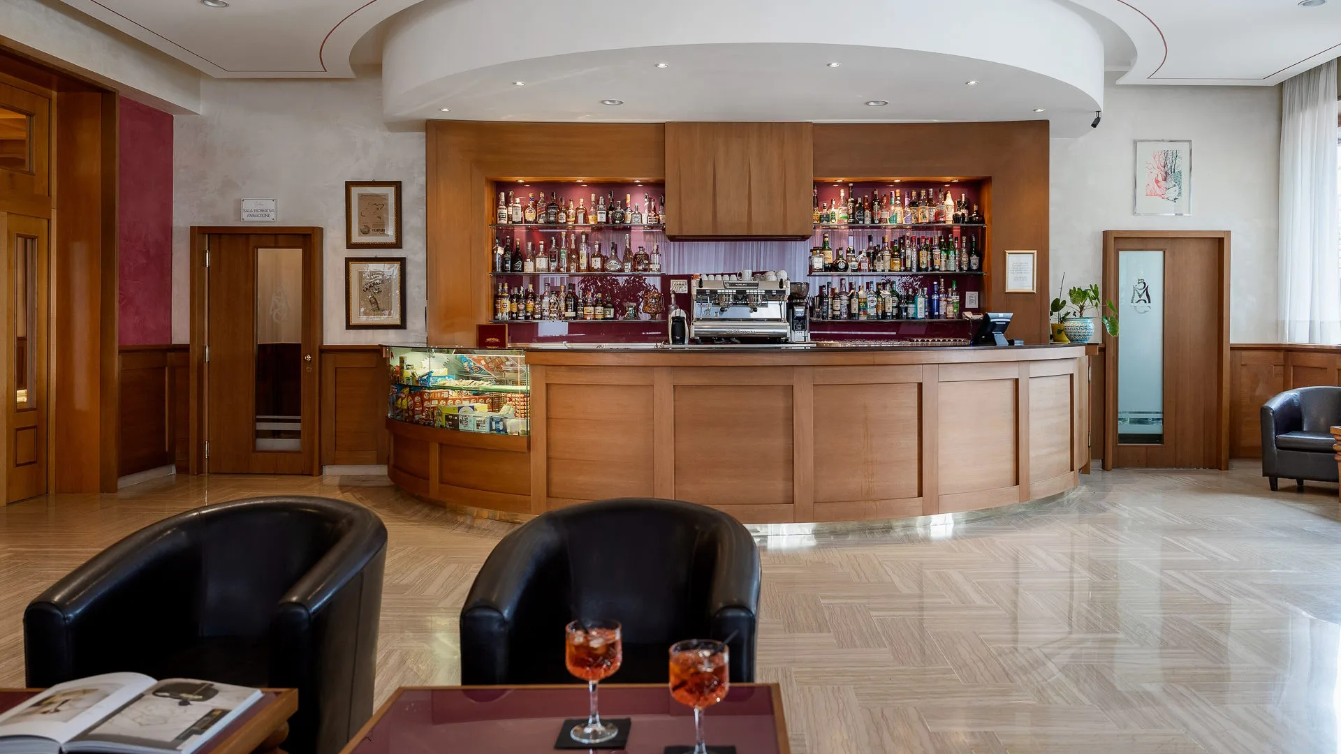 Bar interno dell'hotel con bancone in legno curvo, ampia selezione di liquori e poltrone in pelle