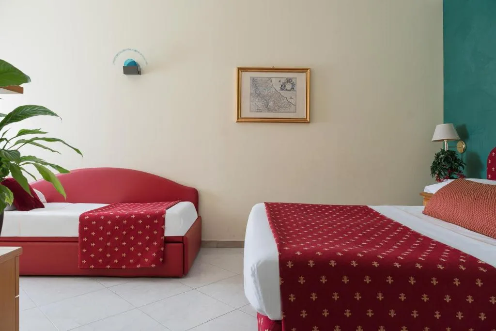 Camera con letto e divano letto rosso, parete verde e scrivania con vasi decorativi