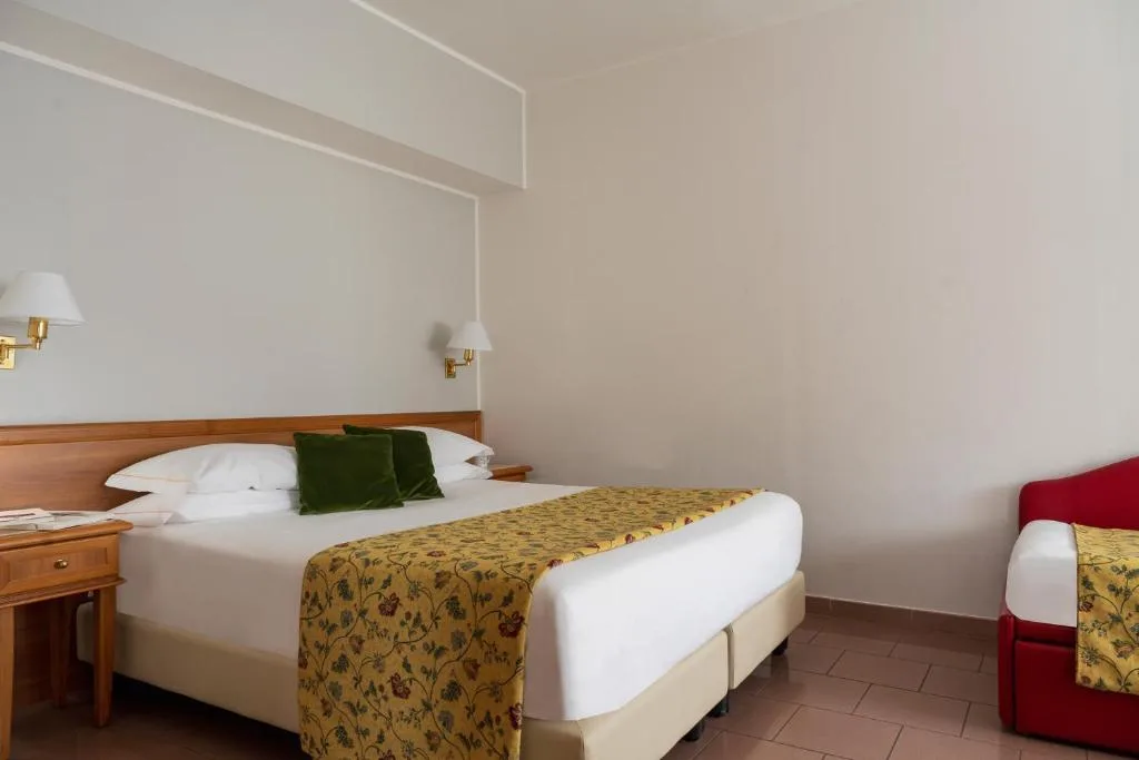 Camera con letto matrimoniale, copriletto floreale giallo, cuscini verdi e poltrona rossa