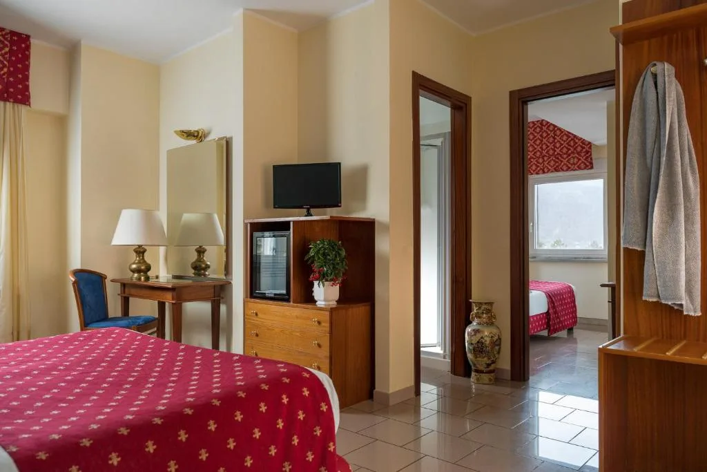 Camera comunicante con letto, TV, cassettiera in legno e vista sulla stanza attigua