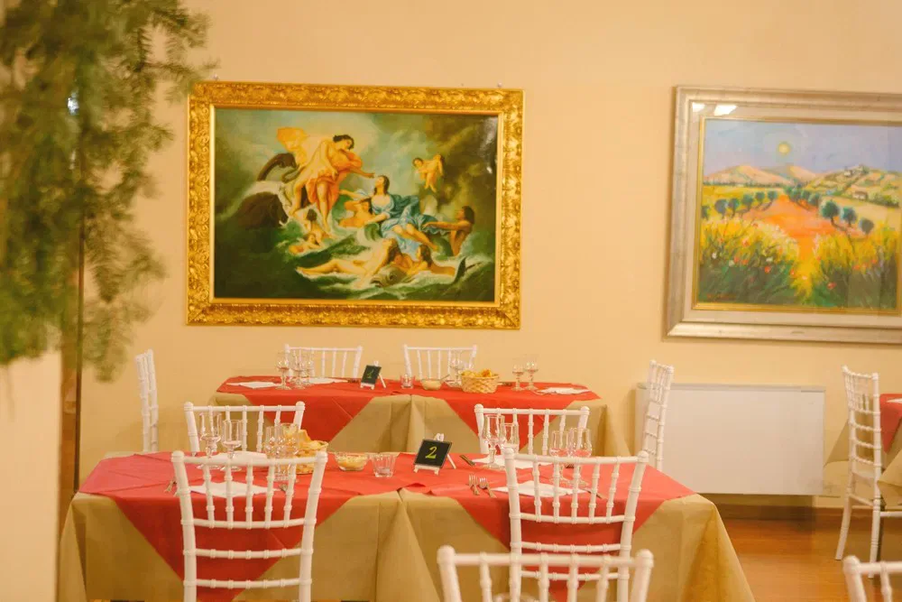 Angolo del ristorante con tavoli apparecchiati e dipinti classici alle pareti gialle