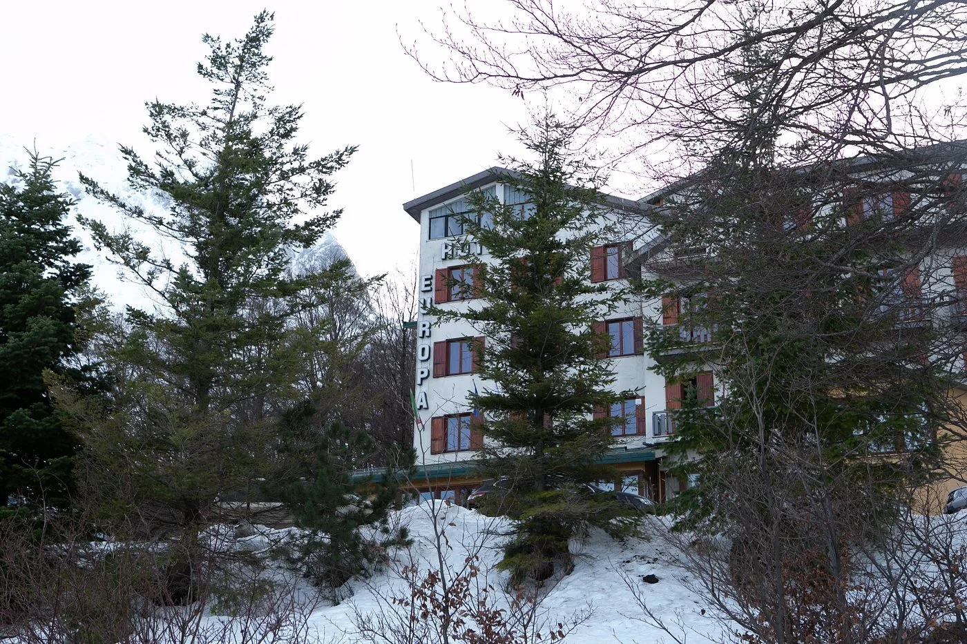 Facciata invernale dell'Hotel Europa tra pini e neve, con montagna sullo sfondo