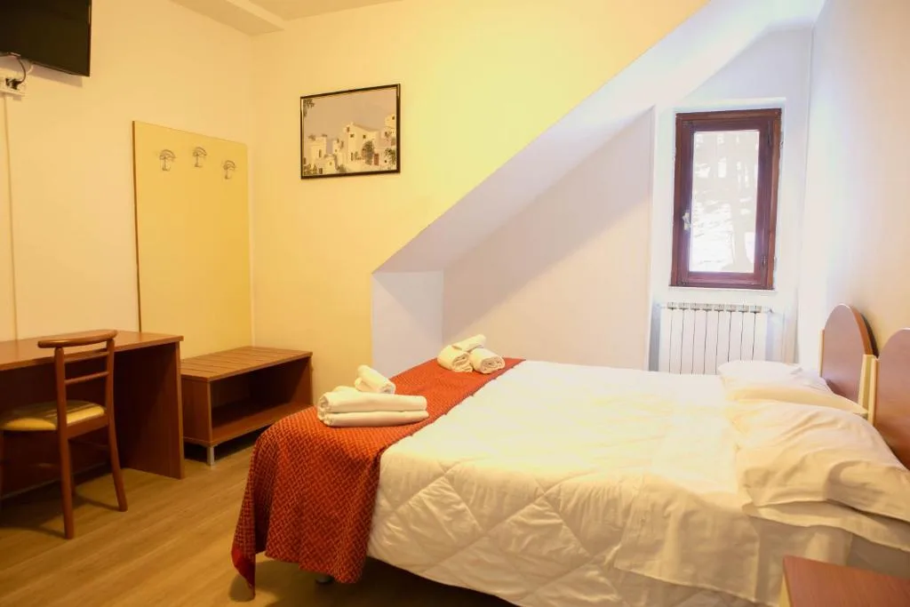 Camera matrimoniale mansardata con letto, coperta arancione, scrivania e finestra