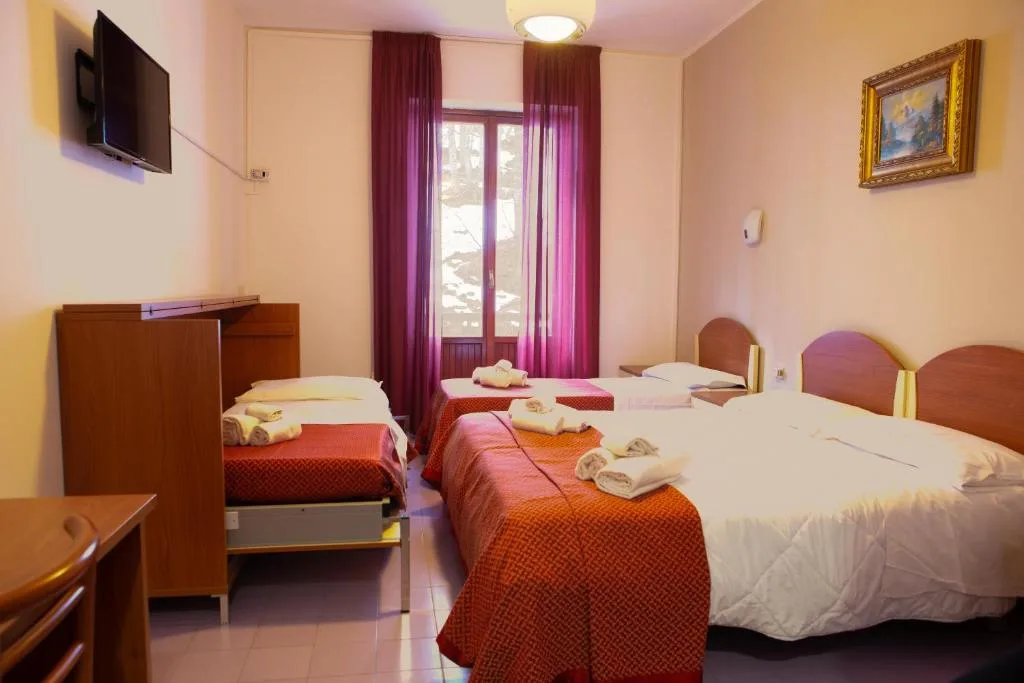 Camera multipla con più letti, coperte arancioni, TV a parete e finestra con tende bordeaux