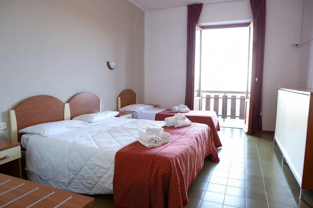 Camera doppia con letti separati, coperte rosse e balcone con porta finestra