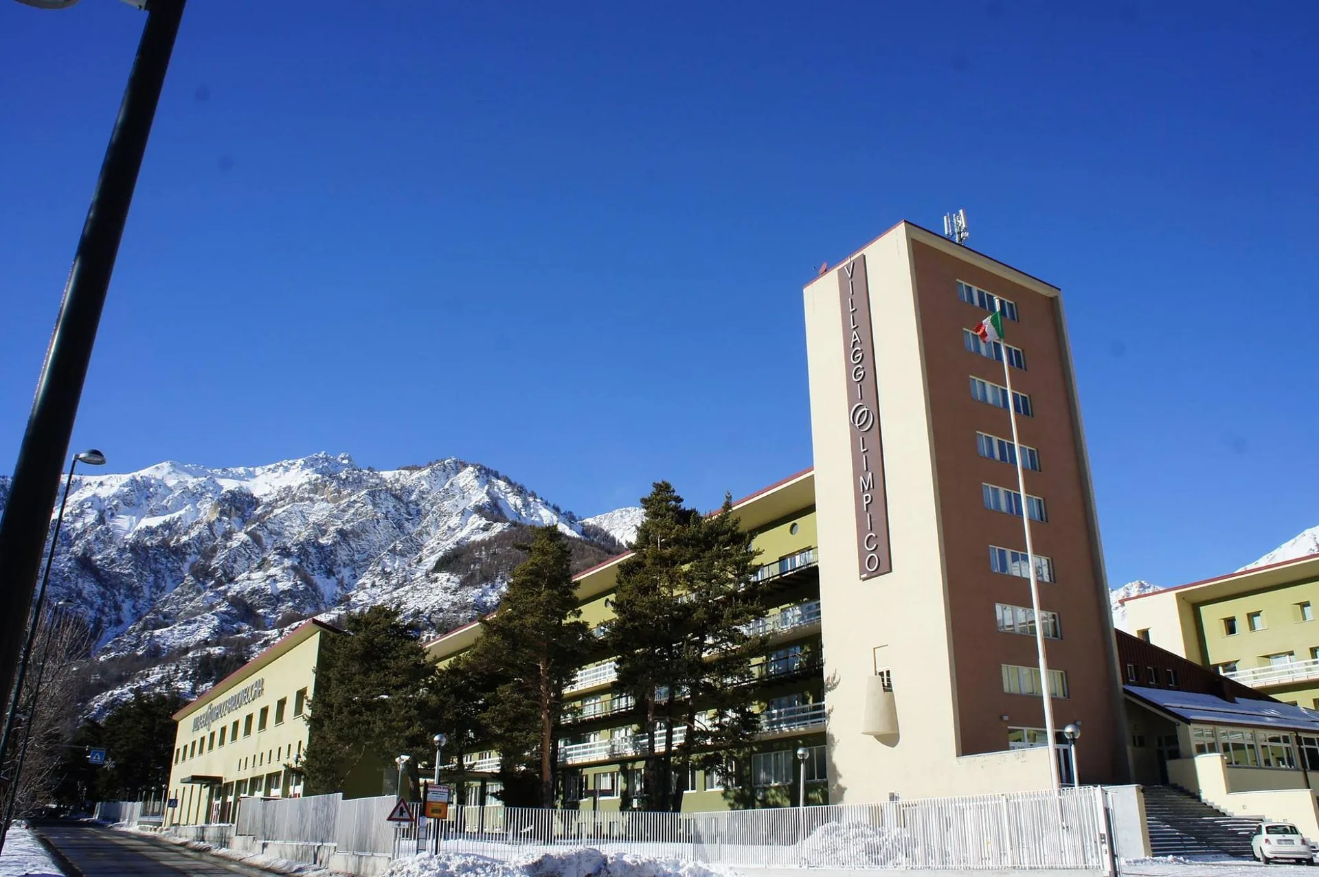 Esterno del Villaggio Olimpico con montagne innevate e bandiera italiana