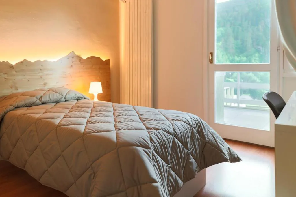 Camera con letto matrimoniale, testiera in legno a forma di montagne e vista bosco