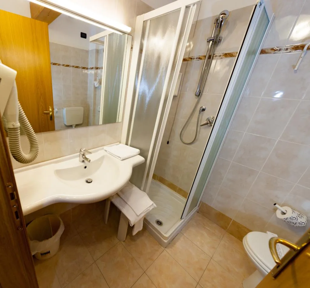 Bagno con lavabo, specchio, box doccia in vetro e piastrelle beige
