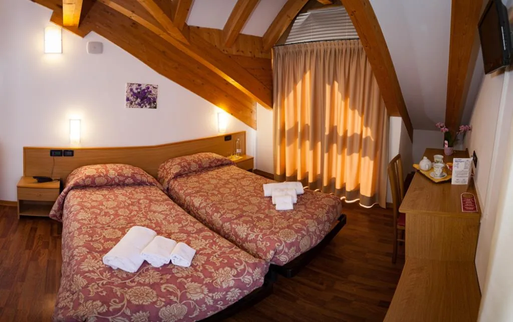 Camera mansardata con travi in legno, letto matrimoniale, scrivania e luce calda dalla finestra