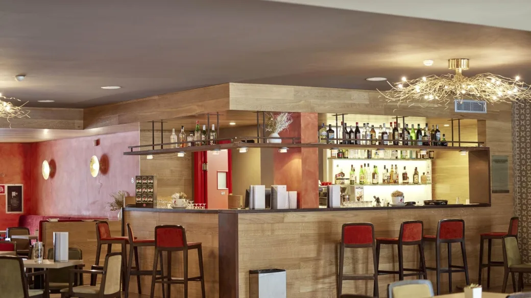 Bar dell'hotel con bancone in legno, sgabelli alti e bottiglie esposte