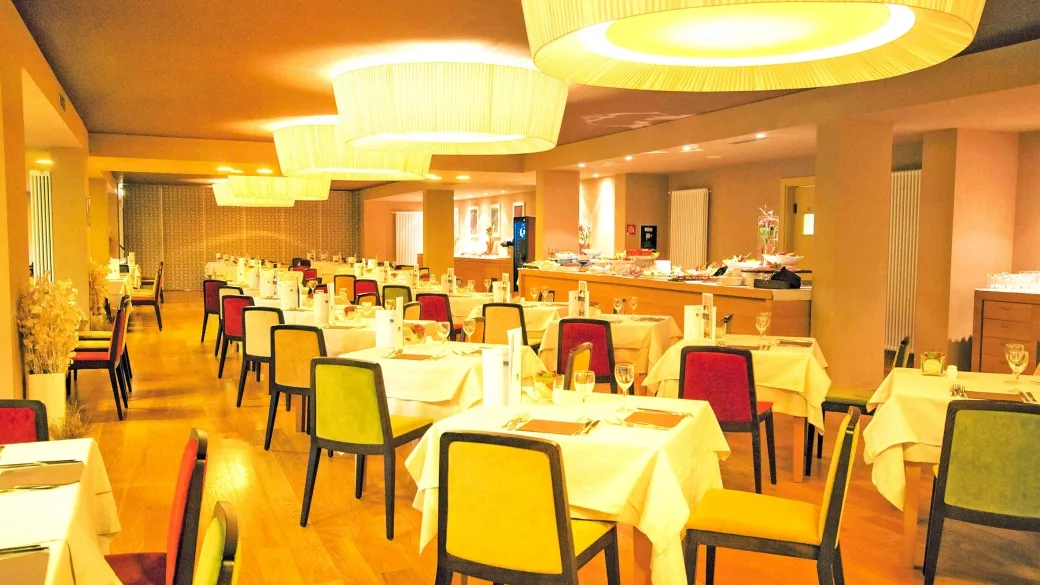 Sala ristorante con tavoli apparecchiati, sedie colorate e ampie lampade a sospensione