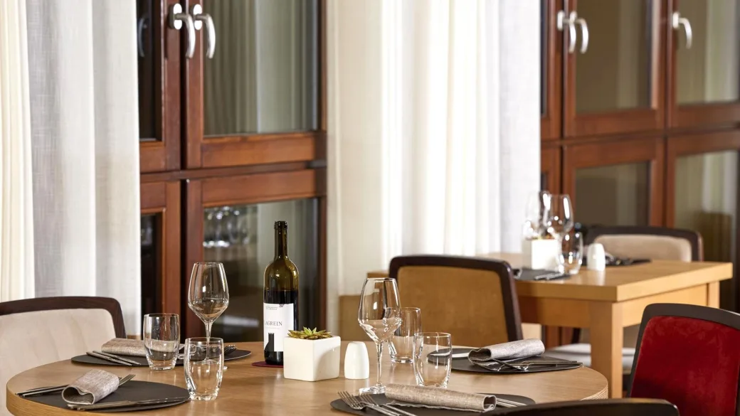 Dettaglio di un tavolo del ristorante apparecchiato con calici, posate e bottiglia di vino