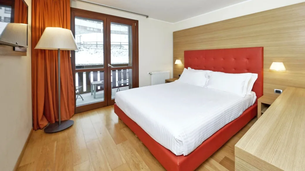 Camera matrimoniale con testiera rossa, parquet e balcone affacciato sulla neve