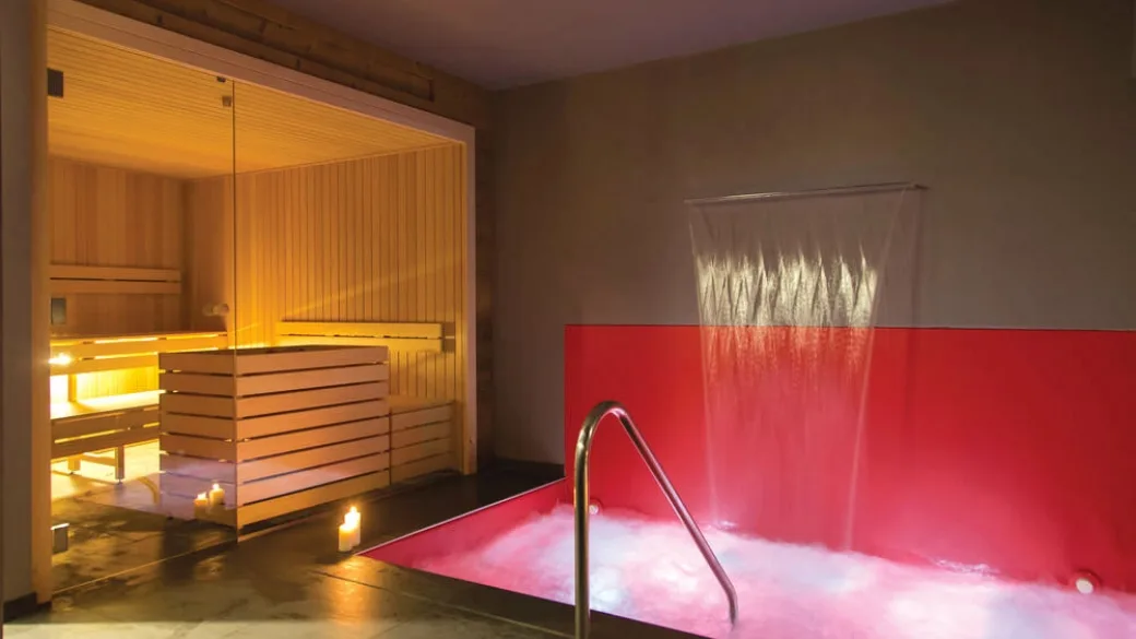 Area spa con sauna in legno e vasca idromassaggio con cascata e illuminazione rossa